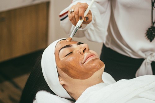Profissional fazendo massagem facial em cliente deitada com toalha branca